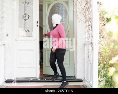 Regno Unito, Sutton, donna con foulard e abbigliamento sportivo che lascia casa Foto Stock