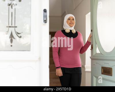 Regno Unito, Sutton, donna con foulard e abbigliamento sportivo che lascia casa Foto Stock