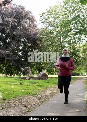 UK, Sutton, donna con il velo che fa jogging nel parco Foto Stock