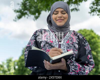 Regno Unito, Sutton, Ritratto di donna con foulard che scrive su notebook all'aperto Foto Stock