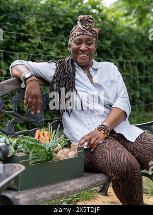 Ritratto di donna sorridente che riposa sulla panchina dopo aver lavorato in giardino Foto Stock