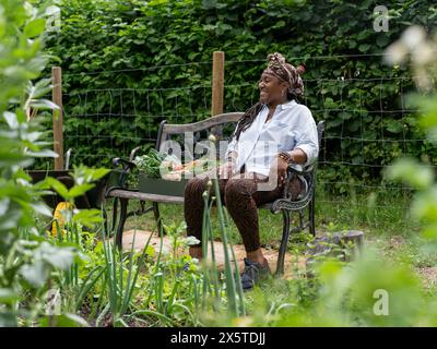 Donna sorridente che riposa sulla panchina dopo aver lavorato in giardino Foto Stock