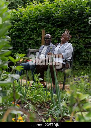 Ritratto di coppia sorridente che riposa sulla panchina dopo aver lavorato in giardino Foto Stock