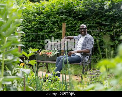 Uomo sorridente maturo che riposa sulla panchina dopo aver lavorato in giardino Foto Stock