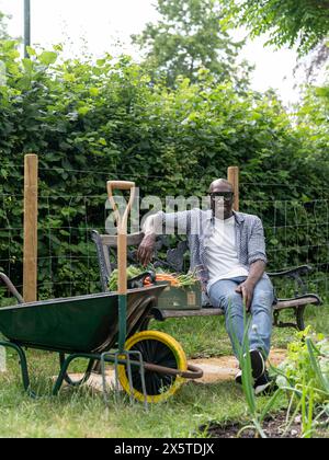 Uomo sorridente maturo che riposa sulla panchina dopo aver lavorato in giardino Foto Stock