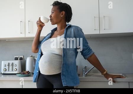 Donna incinta bere il tè in cucina Foto Stock