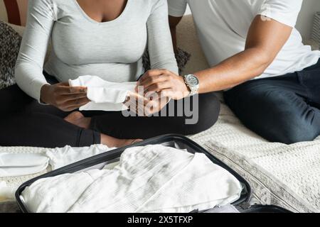 Donna incinta e uomo che tengono a letto vestiti per bambini Foto Stock