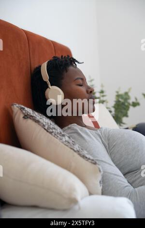 Donna incinta con cuffie che si rilassano sul letto Foto Stock