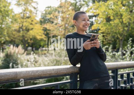 Donna atletica sorridente con smartphone sulla passerella Foto Stock