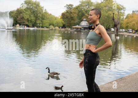 Donna atletica con cuffie in piedi accanto al laghetto nel parco Foto Stock