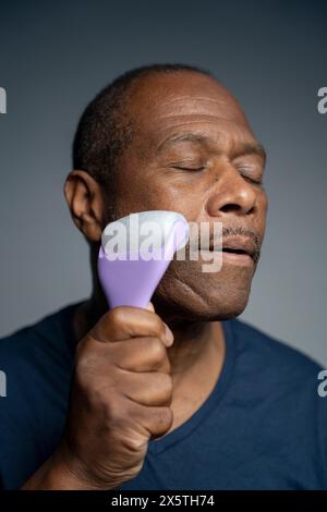 Ritratto di un uomo che fa un massaggio facciale con il rullo Foto Stock
