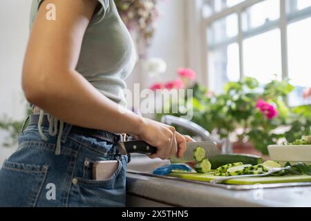 Sezione centrale di una giovane donna che trita verdure in cucina Foto Stock