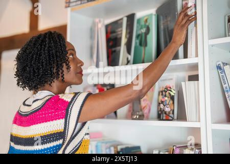 Donna premurosa che sceglie il libro dallo scaffale di casa Foto Stock