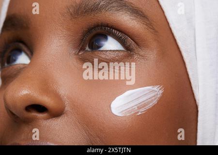 Foto di studio di una giovane donna in hijab bianco che applica la crema per il viso Foto Stock