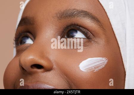 Foto di studio di una giovane donna in hijab bianco che applica la crema per il viso Foto Stock