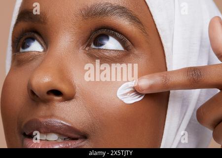 Foto di studio di una giovane donna in hijab bianco che applica la crema per il viso Foto Stock