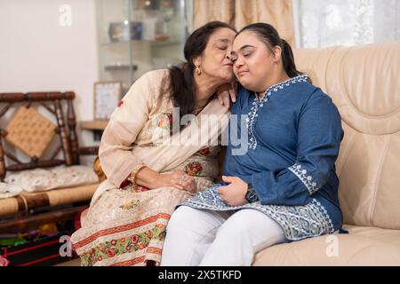 Ritratto di una donna anziana che bacia la nipote della sindrome di Down in salotto Foto Stock