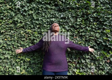 Ritratto di una bella donna con dreadlock davanti al muro dell'edera Foto Stock