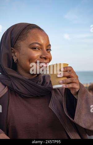 Donna musulmana sorridente che beve caffè Foto Stock