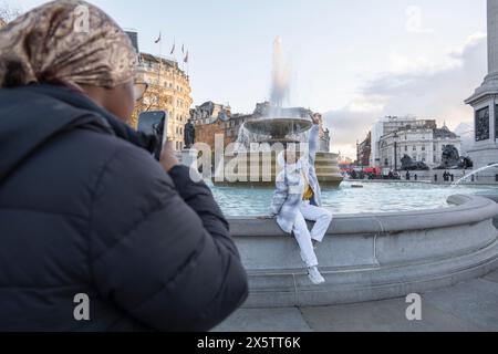 Regno Unito, Londra, giovane donna in hijab che fotografa un amico seduto sulla fontana Foto Stock