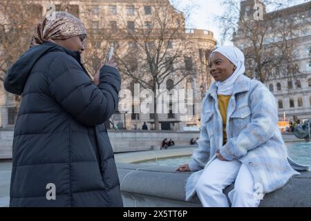 Regno Unito, Londra, giovane donna in hijab che fotografa un amico seduto sulla fontana Foto Stock