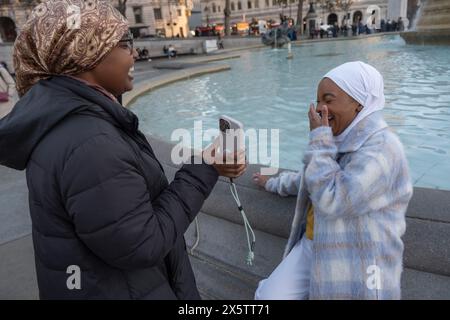 Regno Unito, Londra, giovane donna in hijab che fotografa un amico seduto sulla fontana Foto Stock