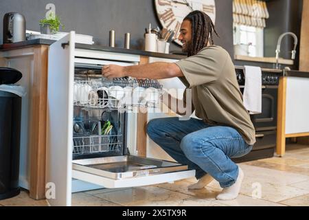 Uomo con paura accovacciato accanto alla lavastoviglie aperta Foto Stock