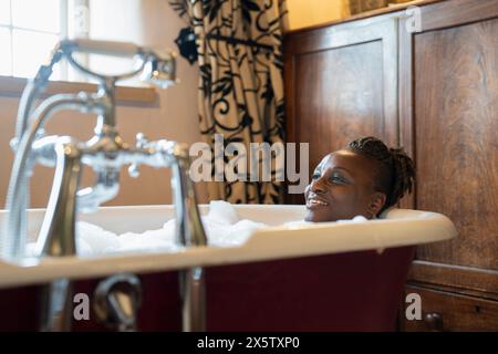 Donna anziana sorridente che fa un bagno di bolle Foto Stock