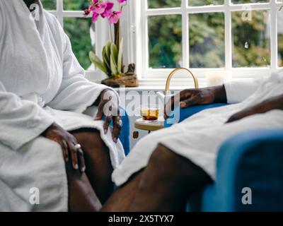 Regno Unito, coppia matura in accappatoi bianchi seduti in poltrone nel centro benessere, sezione intermedia Foto Stock