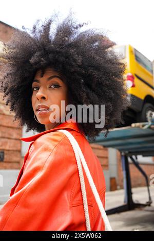 USA, Ritratto di donna con capelli afro che indossa un cappotto di pelle rosso in città Foto Stock