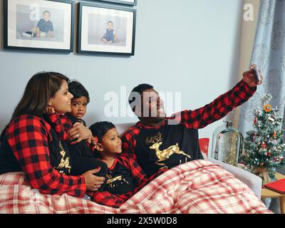 Genitori con figli seduti a letto a fare selfie Foto Stock