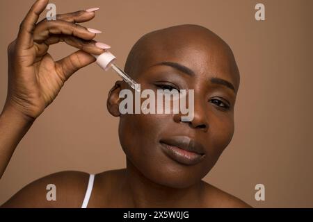 Ritratto in studio di una donna con la testa rasata che applica olio sul viso Foto Stock
