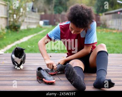 Ragazza che rimuove le scarpe da calcio sul patio Foto Stock