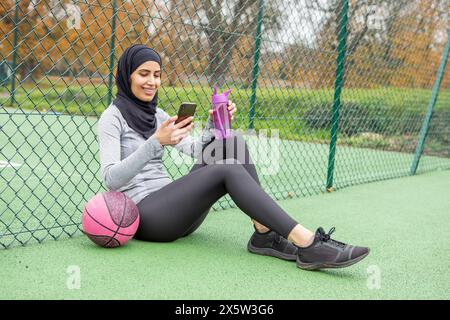 Donna in hijab con palla da basket seduta sul campo da basket Foto Stock