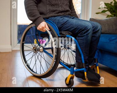La parte bassa di un uomo disabile seduto su una sedia a rotelle a casa Foto Stock