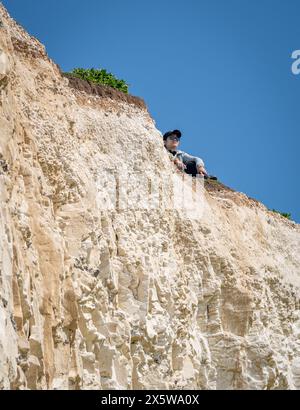 Beachy Head, East Sussex, Regno Unito. 11 maggio 2024. Un turista siede sul bordo della scogliera che si sgretola a 3oo piedi sulla costa vicino a Birling Gap, dato che si prevede che la temperatura raggiunga i 27C oggi nel weekend più caldo dell'anno finora. Beachy Head, East Sussex, UK Credit: Reppans/Alamy Live News Foto Stock