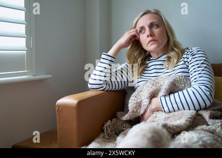 Donna matura economicamente inattiva che soffre di malattia a lungo termine seduta sul divano a casa Foto Stock