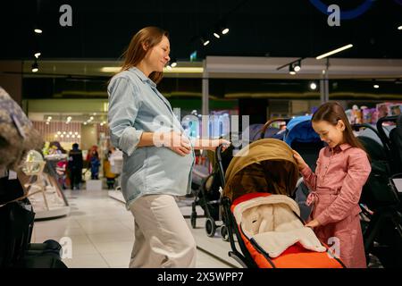 La madre incinta e la bambina scelgono un passeggino nel centro commerciale Foto Stock