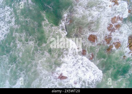 schiuma dalle onde che si infrangono su una costa rocciosa, vista dall'alto aerea con drone Foto Stock