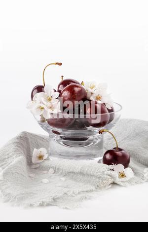 Ciliegie fresche e fiori di ciliegio disposti in una ciotola di vetro Foto Stock