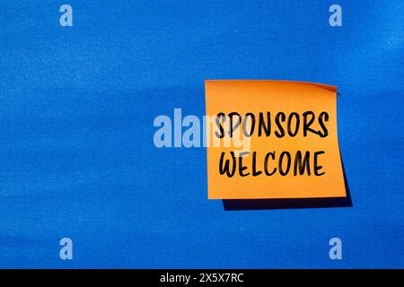 Parole di benvenuto degli sponsor scritte su un adesivo di carta arancione con sfondo blu. Simbolo commerciale concettuale. Copia spazio. Foto Stock