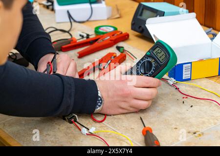 Un uomo che esegue l'assemblaggio elettronico con un misuratore di tensione Foto Stock