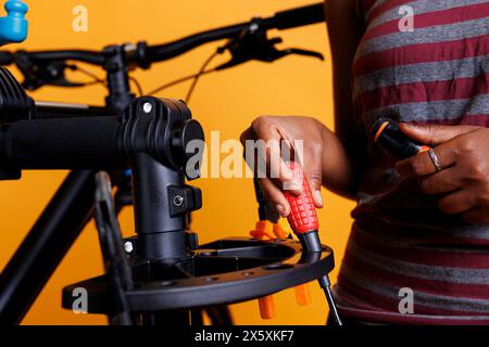 Primo piano della mano afroamericana che organizza gli attrezzi necessari per il servizio di biciclette. La foto si concentra sul cacciavite e su altre attrezzature specializzate che vengono disposte su uno stand di riparazione della bicicletta da parte di un individuo. Foto Stock