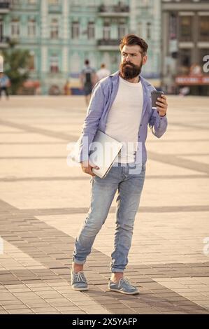 uomo con una comunicazione freelance che tiene un caffè che cammina all'aperto. Foto Stock