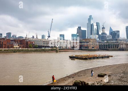 Il Tamigi con la bassa marea con persone che camminano lungo la riva del Tamigi, lo skyline della città di Londra in lontananza, Londra, Inghilterra, 2023 Foto Stock