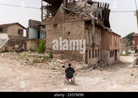 Onur, di fronte al relitto della casa dove abitava in Saray Street, una delle famose località di Hatay. Onur Kaba è un giovane di 22 anni di Hatay, una città più colpita dai terremoti di magnitudo 7,7 e 7,6 che hanno colpito Kahramanmara? Il 6 febbraio 2023. Onur è stato catturato in casa sua ed è rimasto intrappolato sotto le macerie per 87 ore. Dopo essere stato salvato, Onur è stato portato per la prima volta in un ospedale vicino, dove le sue gambe sono state curate per 12 giorni con vari trattamenti per prevenire l'amputazione. Alla fine, ha perso entrambe le gambe e continua la sua vita come amputato. Onur, che vive ancora ad ha Foto Stock