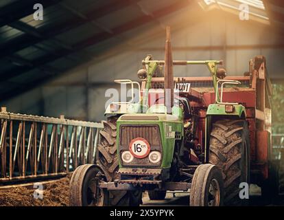 Azienda agricola, macchina e vecchio trattore in stalla con sporcizia, ruggine e polvere in magazzino a terra. Camion d'epoca, retrò e aratro in un capannone abbandonato Foto Stock