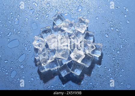 Pile di cubetti di ghiaccio e gocce d'acqua su sfondo blu, vista dall'alto Foto Stock