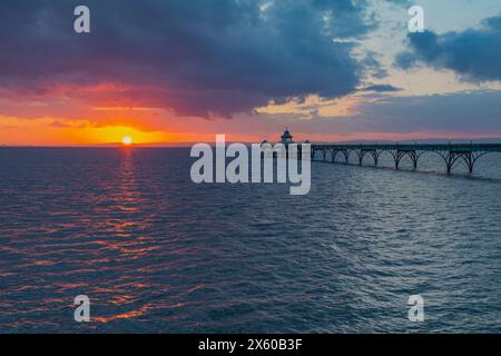 Molo di Clevedon all'orizzonte delle arance giallastro al tramonto e una leggera striscia di luce del sole che attraversa il mare Foto Stock