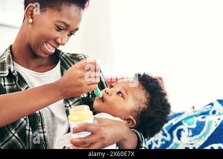Mamma, bimbo e sorrisi a casa con l'alimentazione per nutrizione, vitamine e crescita per lo sviluppo del bambino. Gente di colore, genitore e bambino o bambino con pasto Foto Stock